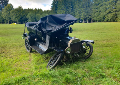 Schwer beschädigter schwarzer Oldtimer steht auf einer Wiese.