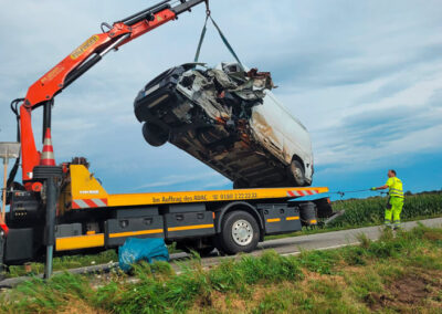Kran lädt einen stark beschädigten, weißen Kleintransporter auf einen ADAC-Abschlepp-LKW.