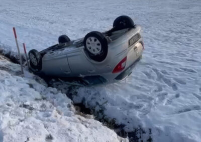 Silbernes Auto liegt überschlagen in einem verschneiten Graben.