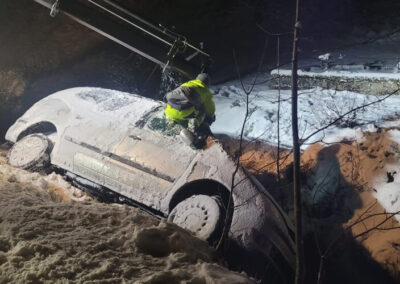 Einsatzkraft sichert ein schneebedecktes, silbernes Auto im Graben.