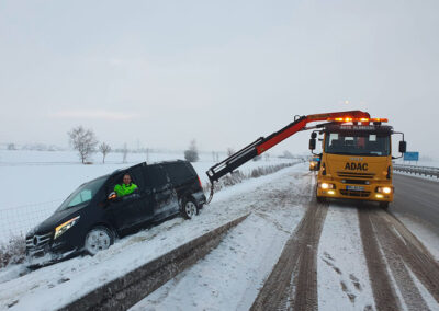 ADAC-Abschlepp-LKW sichert ein Fahrzeug neben einer verschneiten Straße.